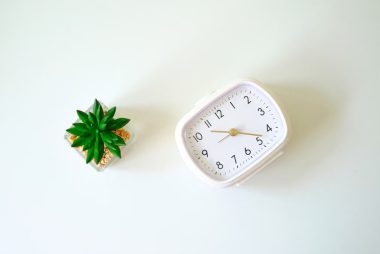 A minimalist desk scene with a white clock and a small cactus plant on a white background.